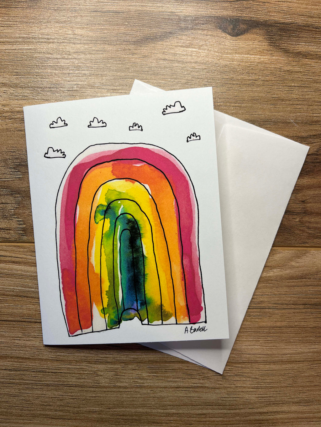 Greeting card with a colorful rainbow illustration and envelope on a wooden surface